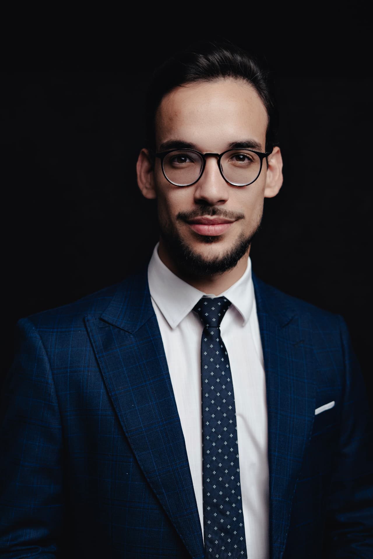 Retrato editorial de Lucian Rabello de terno azul xadrez, camisa branca, gravata e óculos